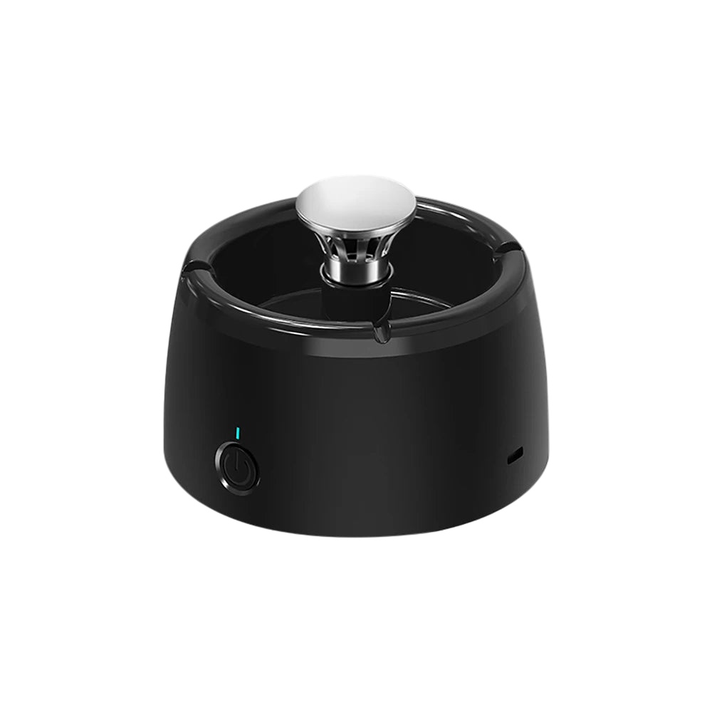 A black PureSmoke Smart Ashtray with air purification features, including a visible filter and a humidifier function, placed on a table in a room with green plants in the background.