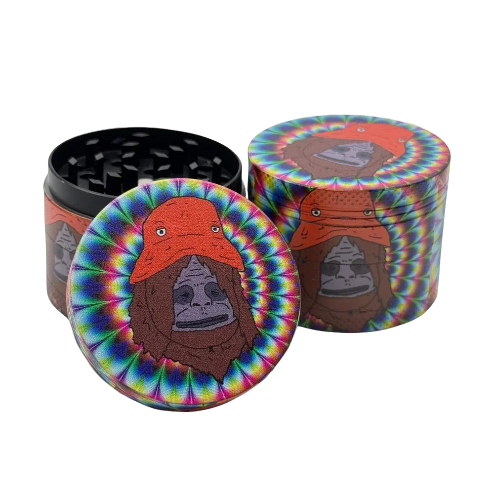 The image displays the Trippy Chimp Crusher, a metal herb grinder featuring a tie-dye pattern and an artistic depiction of a chimpanzee wearing an orange hat on the lid. The grinder is composed of four pieces designed for efficient grinding, with a magnetic lid that ensures a secure seal and a polymer O-ring for smooth operation.