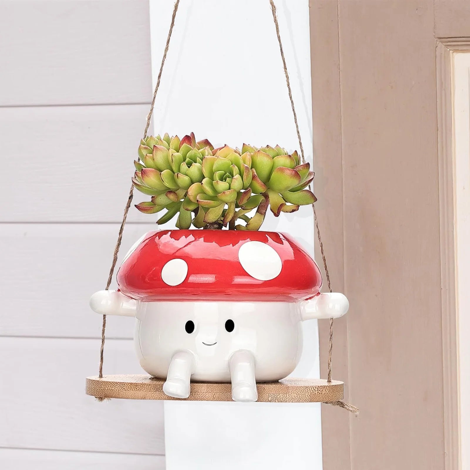 Mushroom-shaped planter with succulents hanging on a rope against a neutral wall.