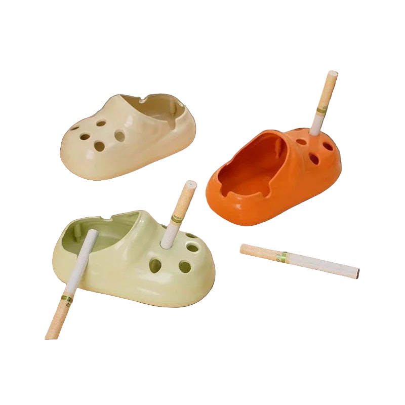 Three croc shoe-shaped ashtrays in different colors on a table with cigarettes inside.
